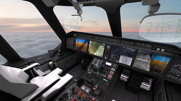 Cockpit of large aircraft showing glass-display avionics systems and a sunset with undercast skies.