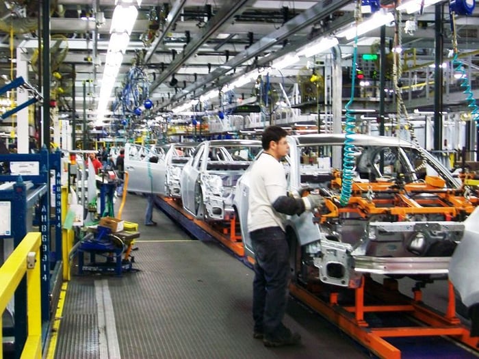 Workers on an automotive assembly line tend to partially-assembled Chevrolet Cruze sedans.