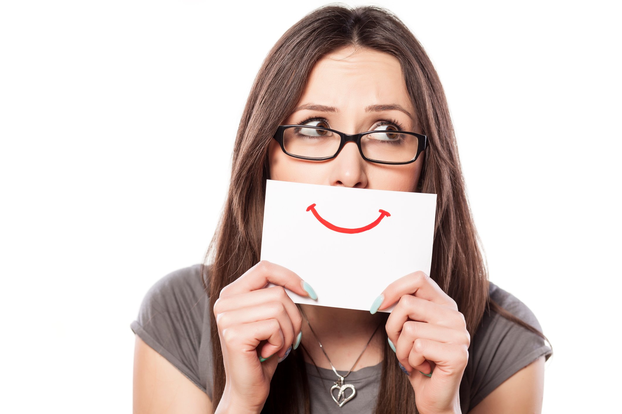 Young woman looking to her left holding a piece of paper with a smile drawn on it over her mouth