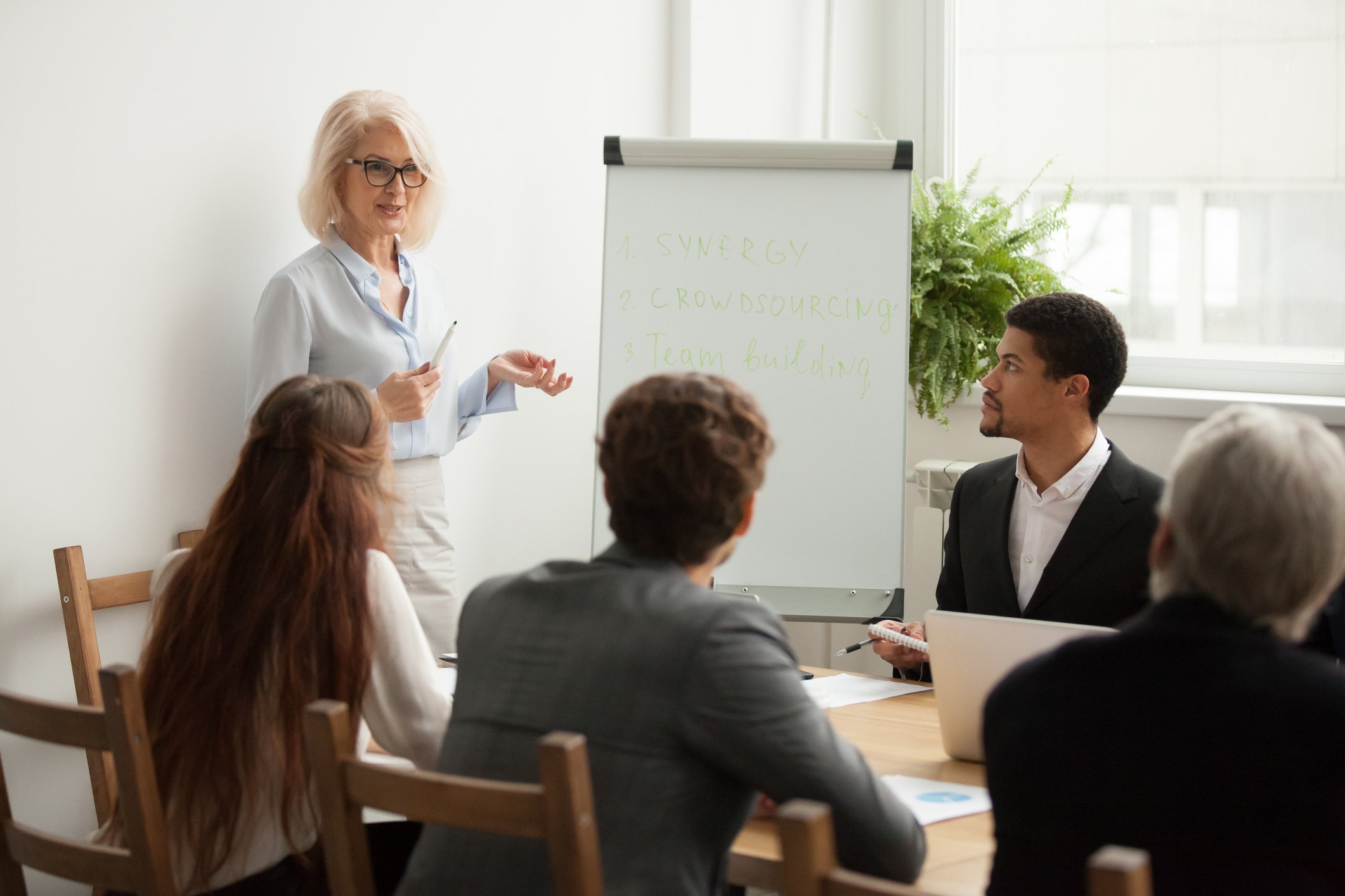 Professionally dressed woman standing and addressing a group of professionals
