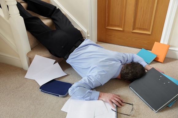 A man lies sprawled at the foot of some stairs, his notebook, tablet, and papers scattered around him.
