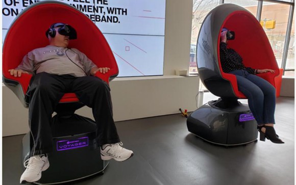 Two people sitting in egg-shaped chairs at Verizon 5G Experience Labs, watching the "First Man" moon landing recreation.