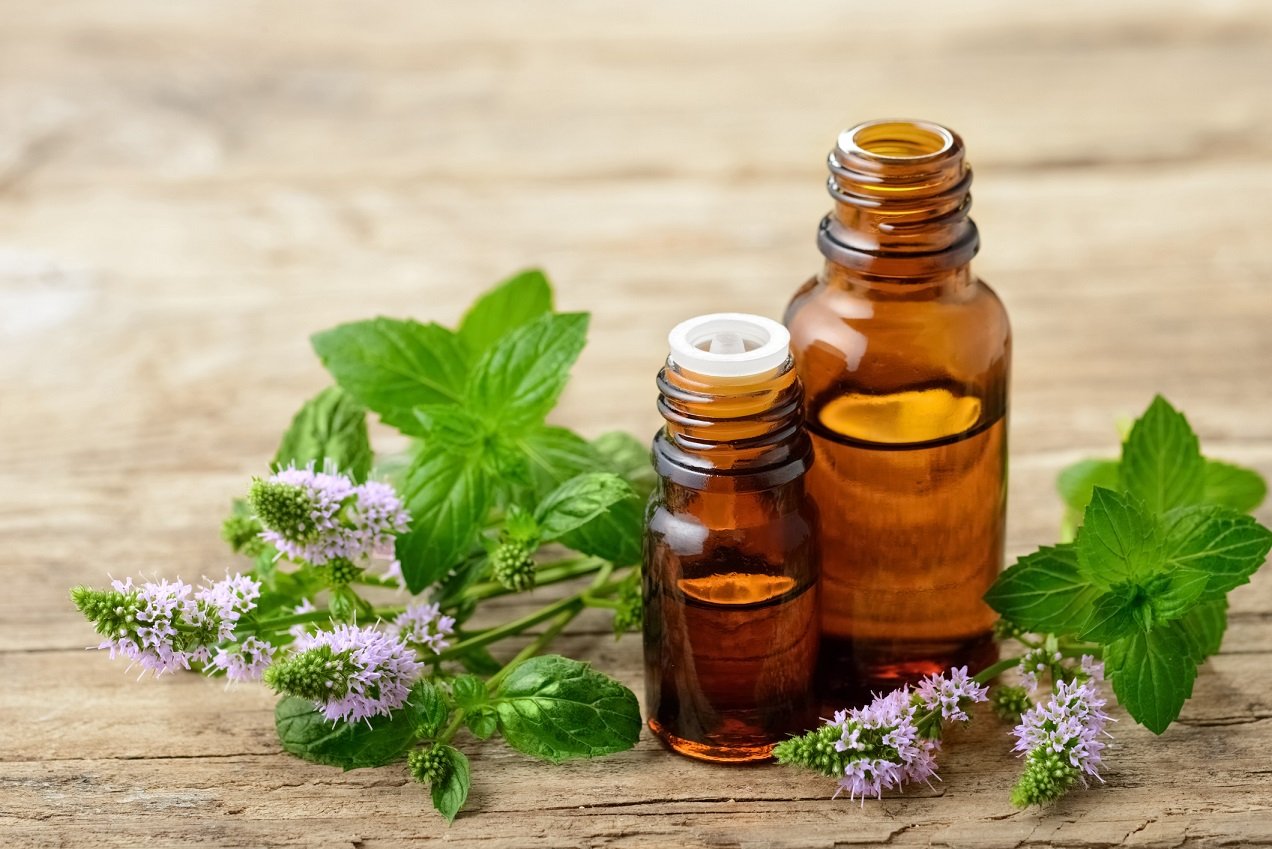 Peppermint leaves next to peppermint oils in glass containers.