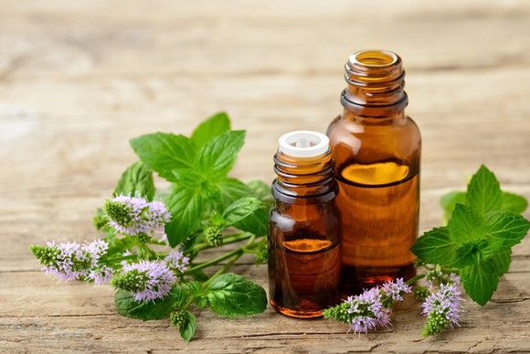 Peppermint leaves next to peppermint oils in glass containers.