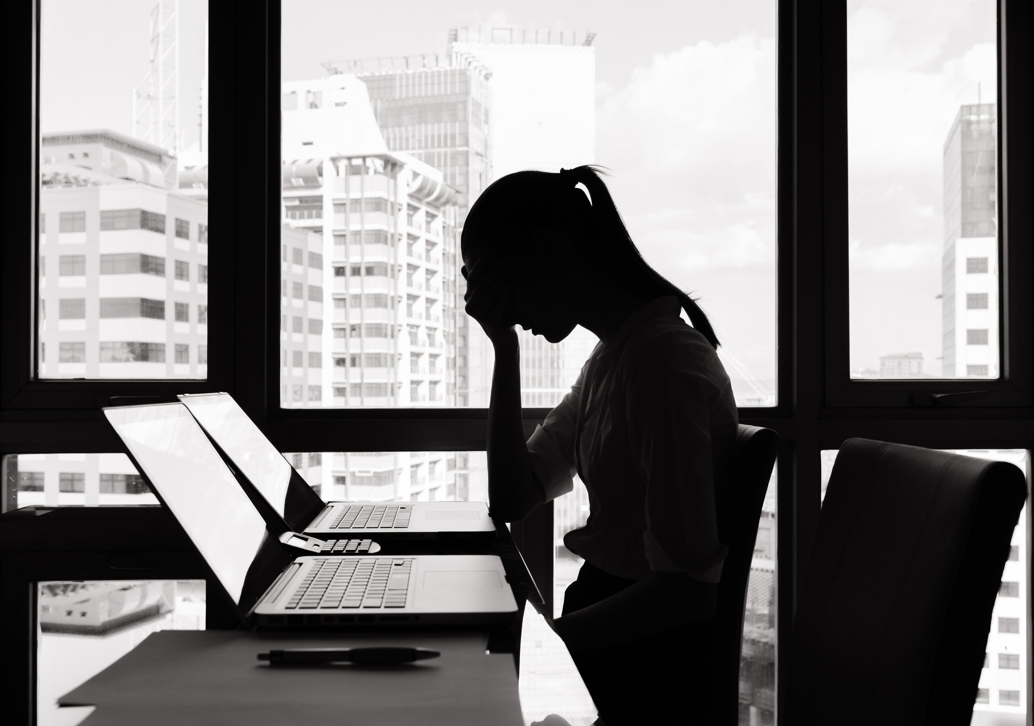 Distressed-looking woman sitting at a table with laptop in front of her.