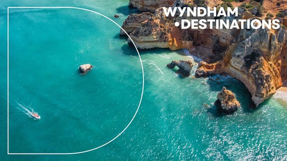 An aerial view of a boat in the water near cliffs along with the text Wyndham Destinations.
