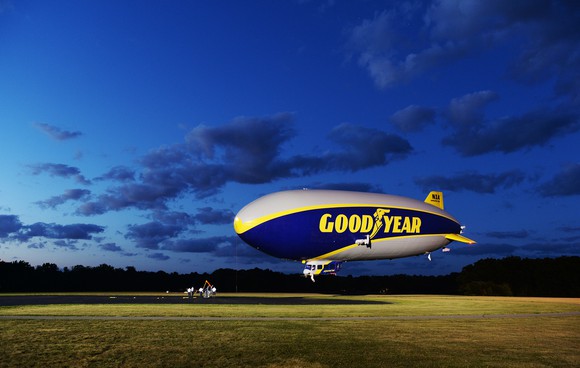 A Goodyear blimp landing in a field in the evening.