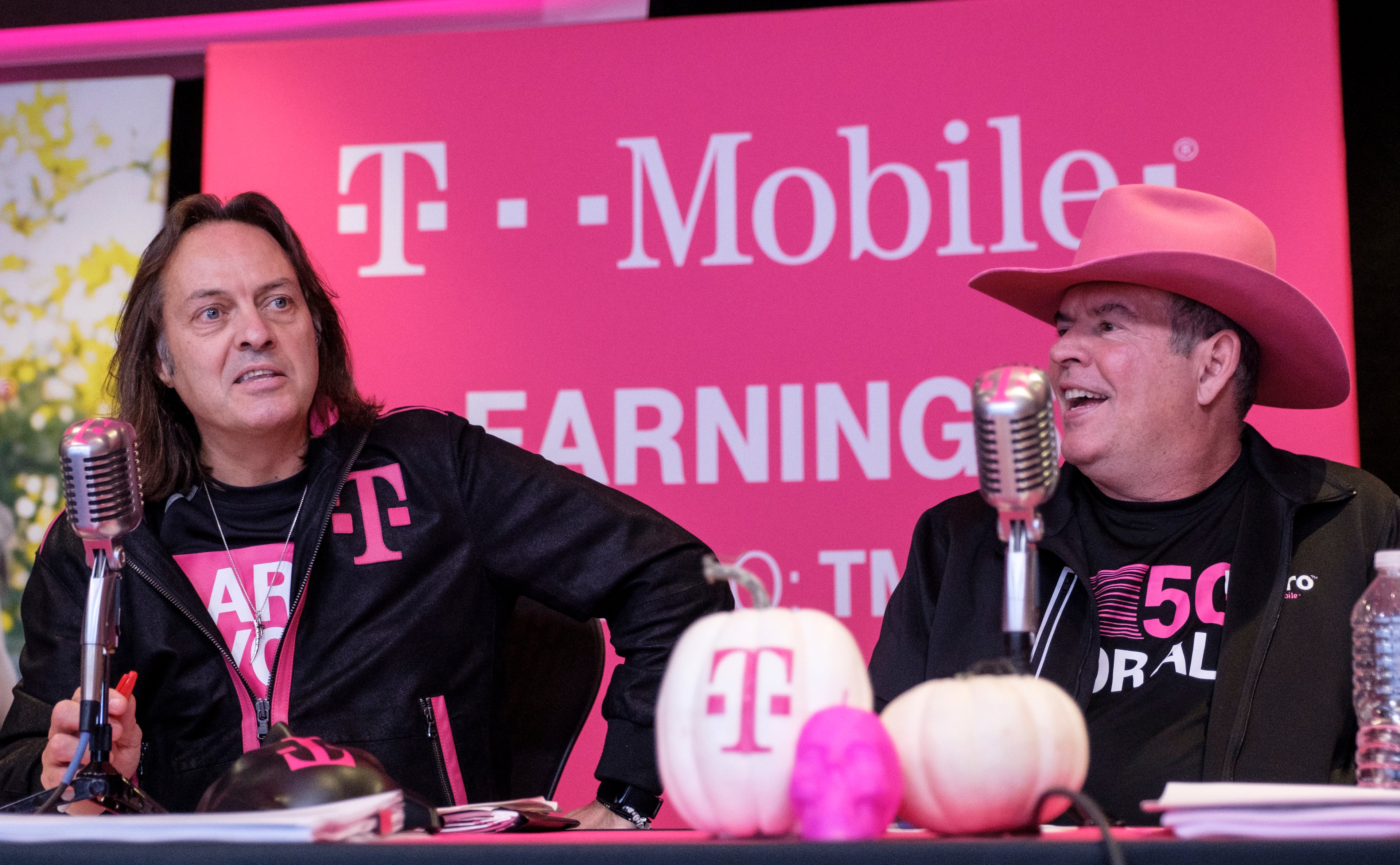 T-Mobile CEO John Legere and CFO Braxton Carter sitting in front of microphones.