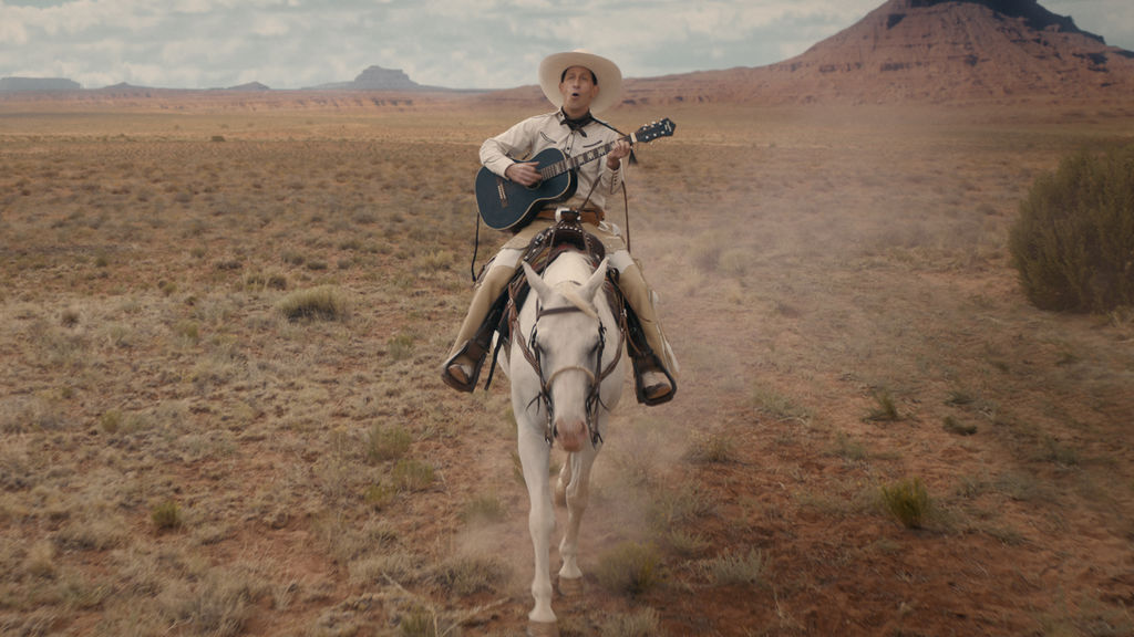 Still image of a cowboy playing guitar on a horse in the desert from "The Ballad of Buster Scruggs"