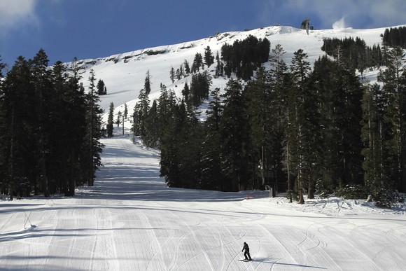 Lone skier on a trail with trees on a snow-covered mountain.