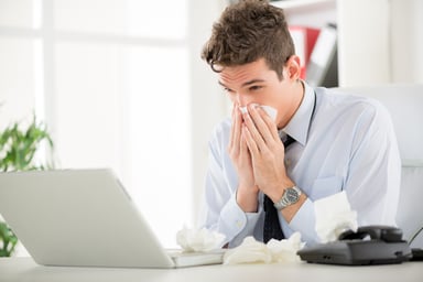 man blowing nose at desk_GettyImages-862313470