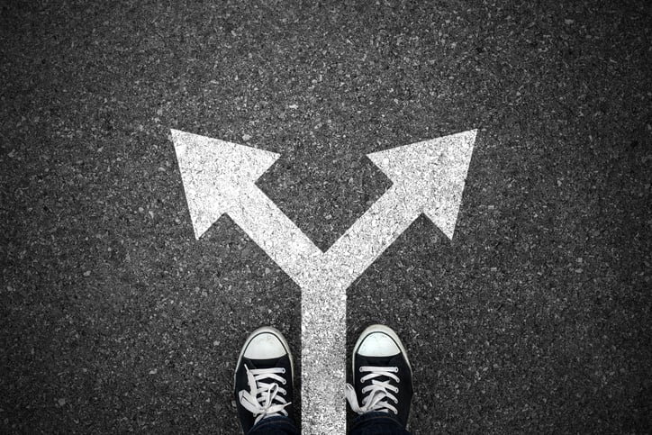 Two shoes in front of an arrow splitting into two directions drawn on the pavement, seen from above