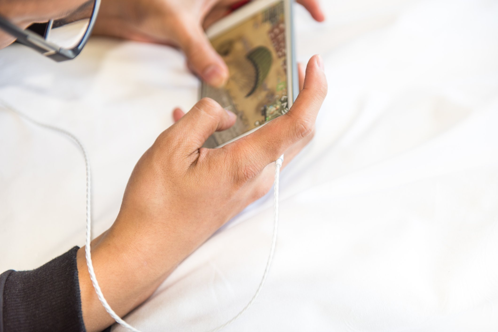 Man lying on a bed while playing a game on a smartphone.