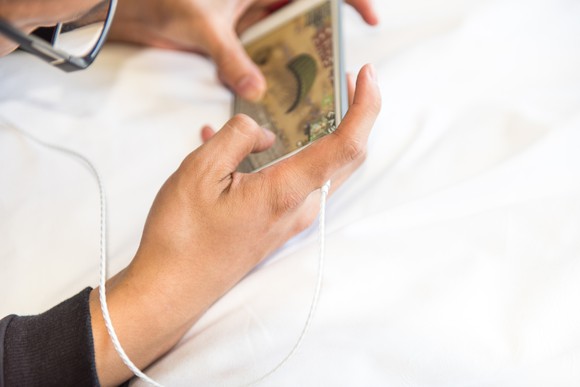 Man lying on a bed while playing a game on a smartphone.