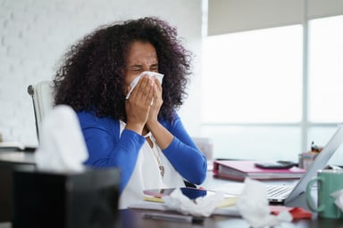 woman blowing nose at desk_GettyImages-967095382