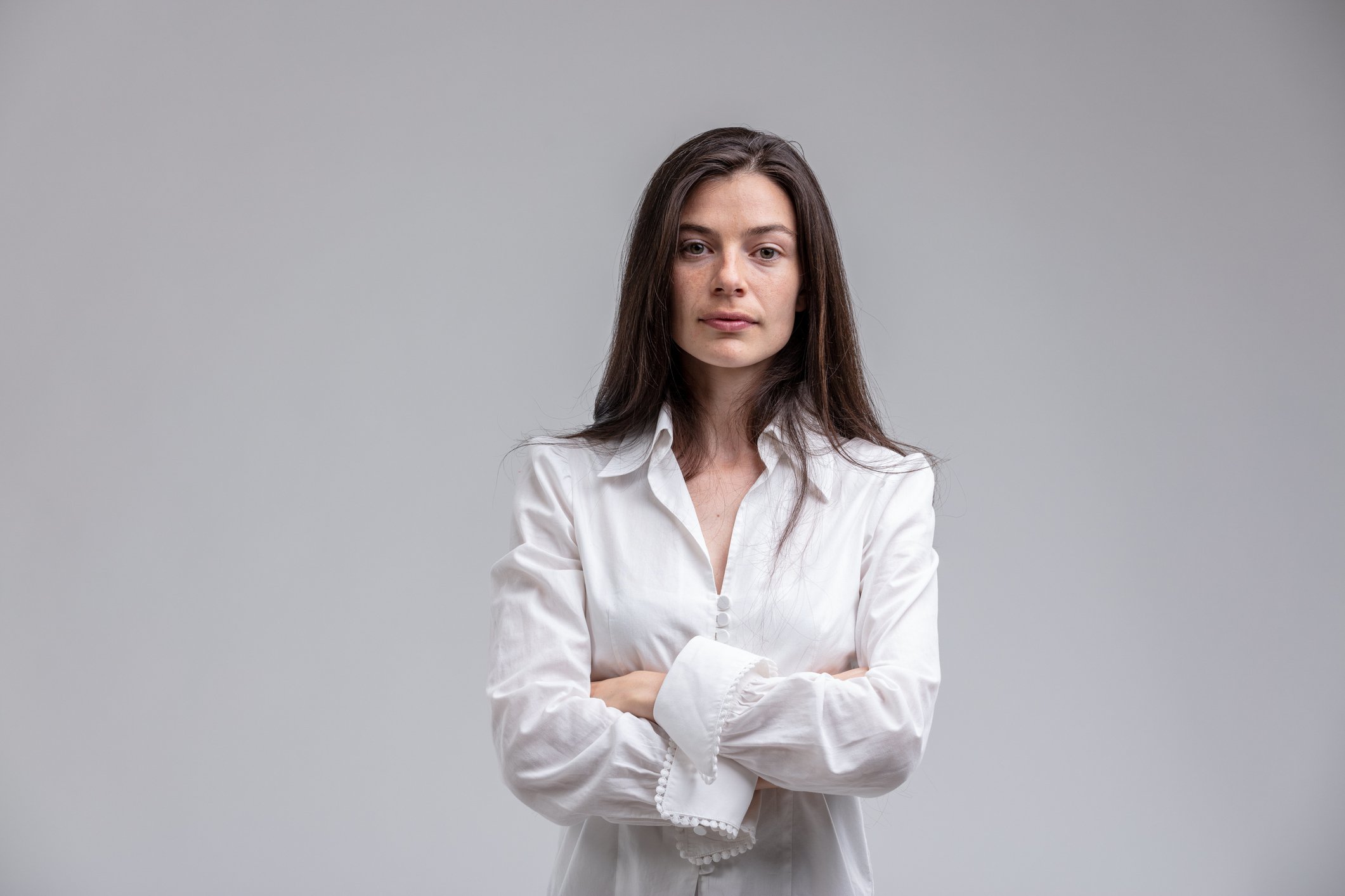 Woman standing with arms crossed against gray background.