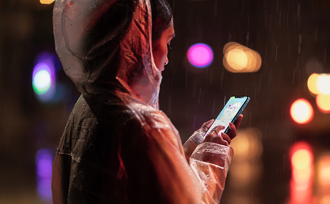 A woman typing on an iPhone XR on a dark street.