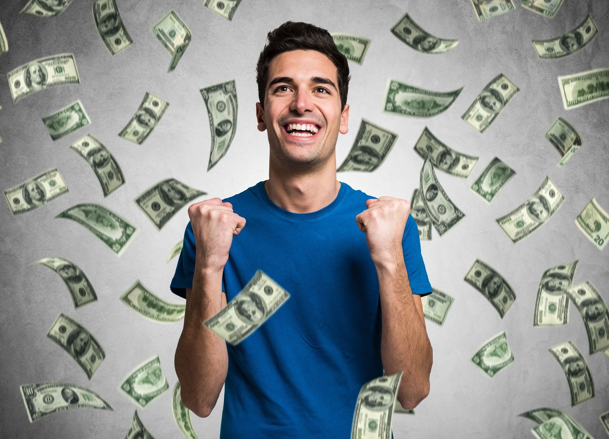 A young man does a double fist pump as dollar bills rain down on him. 