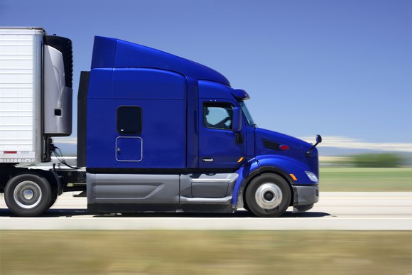 Tractor-trailer with blue cab speeding down a highway.