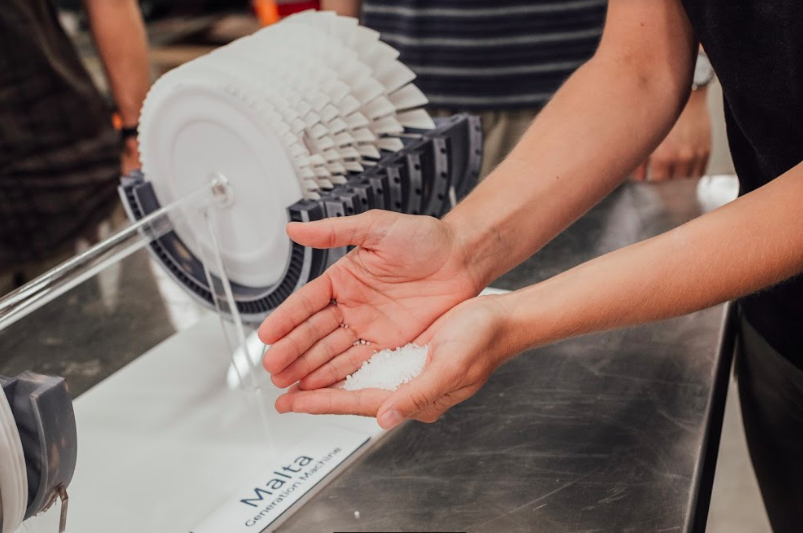 A person holding salt in their palm in front of a device with the Malta name on it