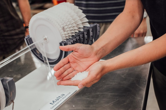 A person holding salt in their palm in front of a device with the Malta name on it