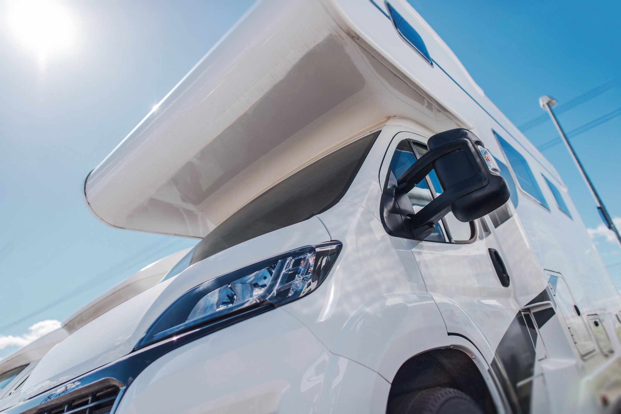 Close-up view of a white camper van in lot under bright sun.
