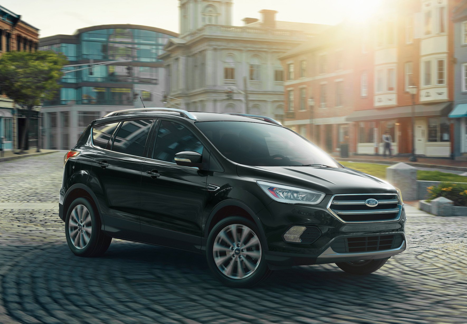 A black Ford Escape, a compact crossover SUV, on a cobblestone road in a town center.