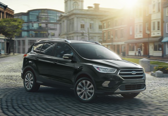 A black Ford Escape, a compact crossover SUV, on a cobblestone road in a town center.