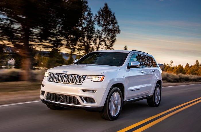 A white Jeep Grand Cherokee, a large crossover SUV, on a country road.