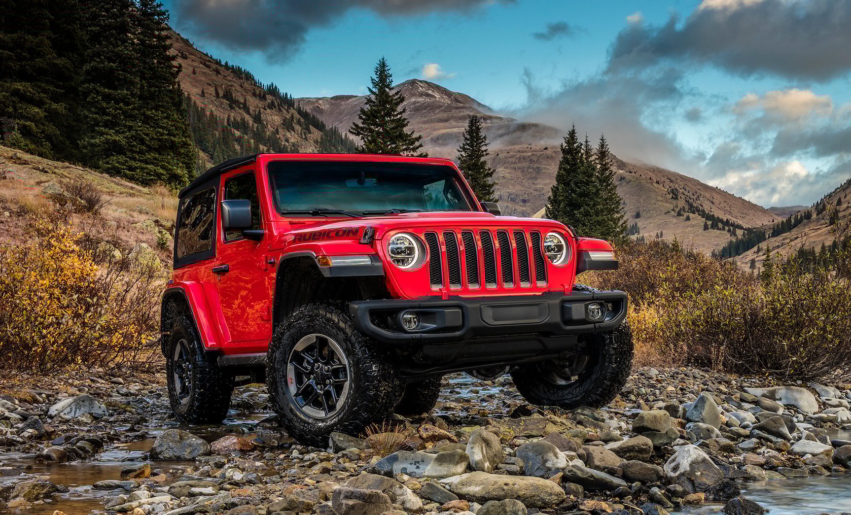 A red Jeep Wrangler Rubicon on a gravel road in the mountains.