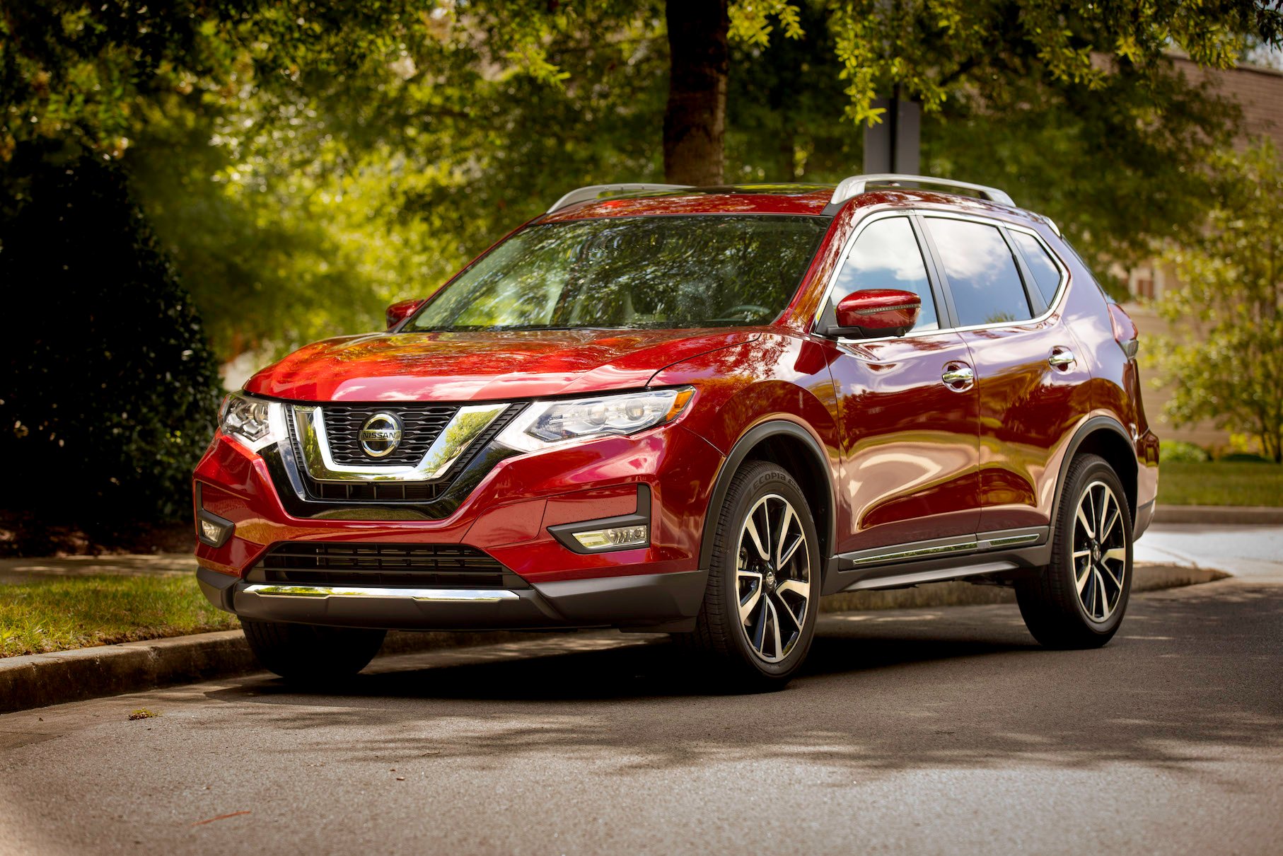A red Nissan Rogue, a compact crossover SUV. parked on a leafy street.