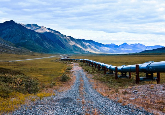 Pipeline running alongside a gravel road with mountains in the background