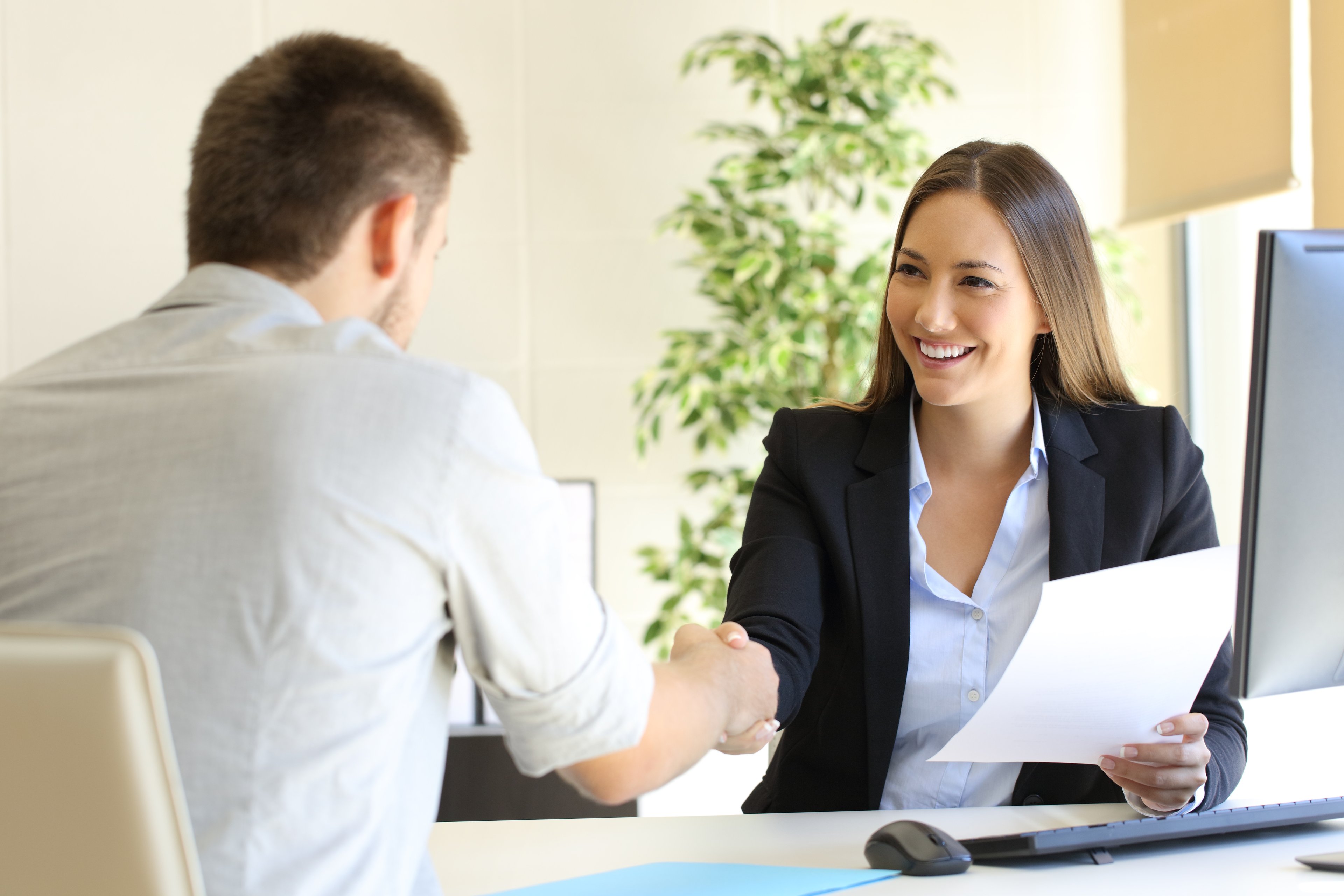 Woman holding piece of paper and shaking hands with man sitting across from her.