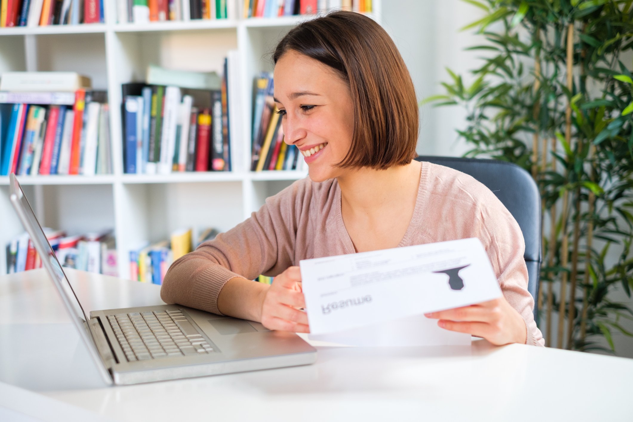 Woman at laptop smiling and holding document