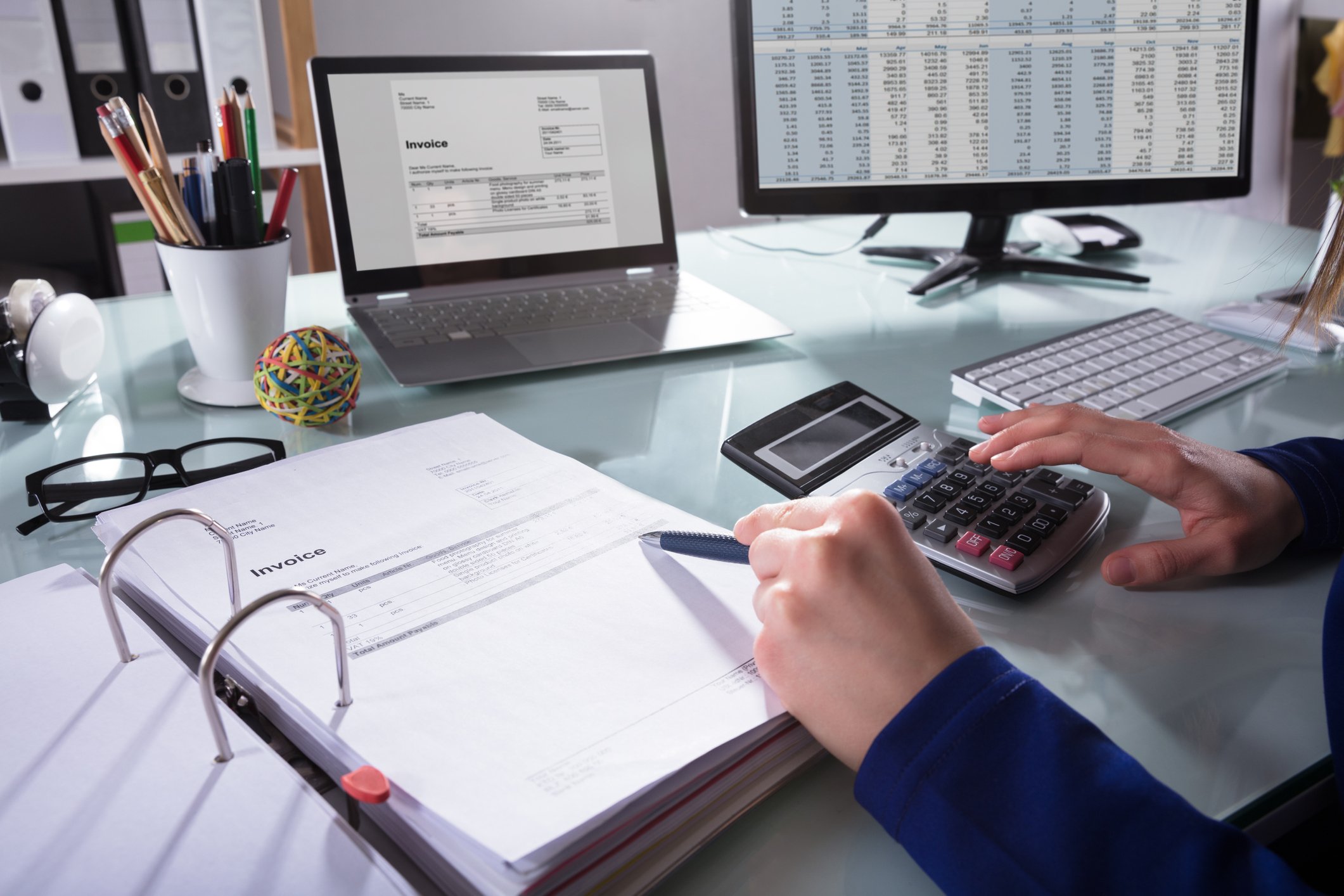 Hands with pen and calculator in front of computer monitor and laptop