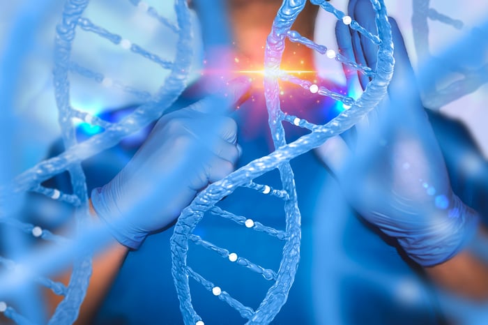 Large image of DNA helix with physician standing behind it holding his finger up to a strand with a bright light appearing on it