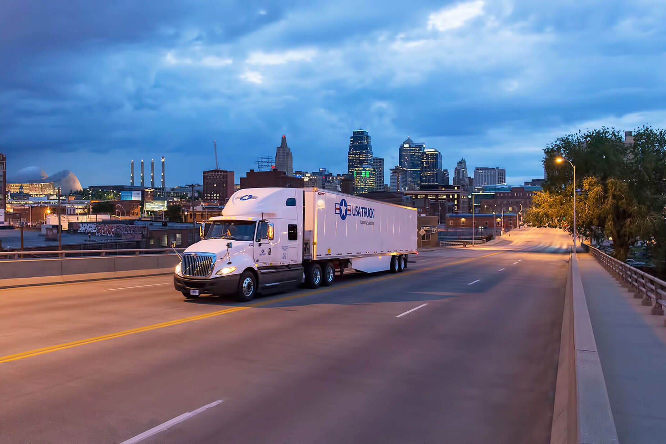 A USA Truck tractor trailer drives in front of a city skyline.