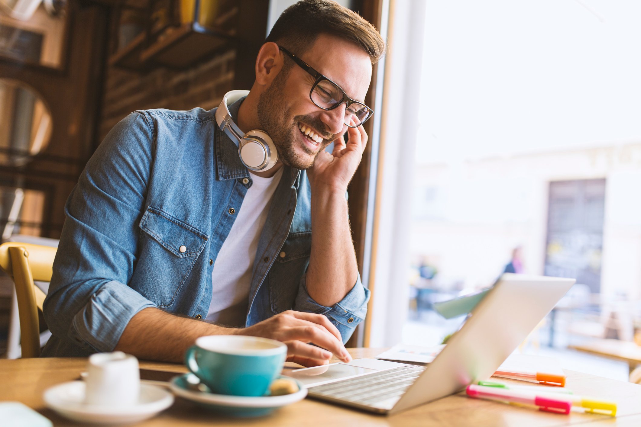 Man with headphones around neck typing on laptop in coffee shop