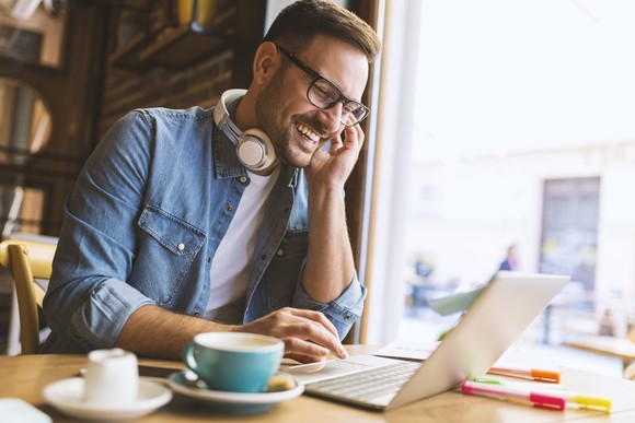 Man with headphones around neck typing on laptop in coffee shop