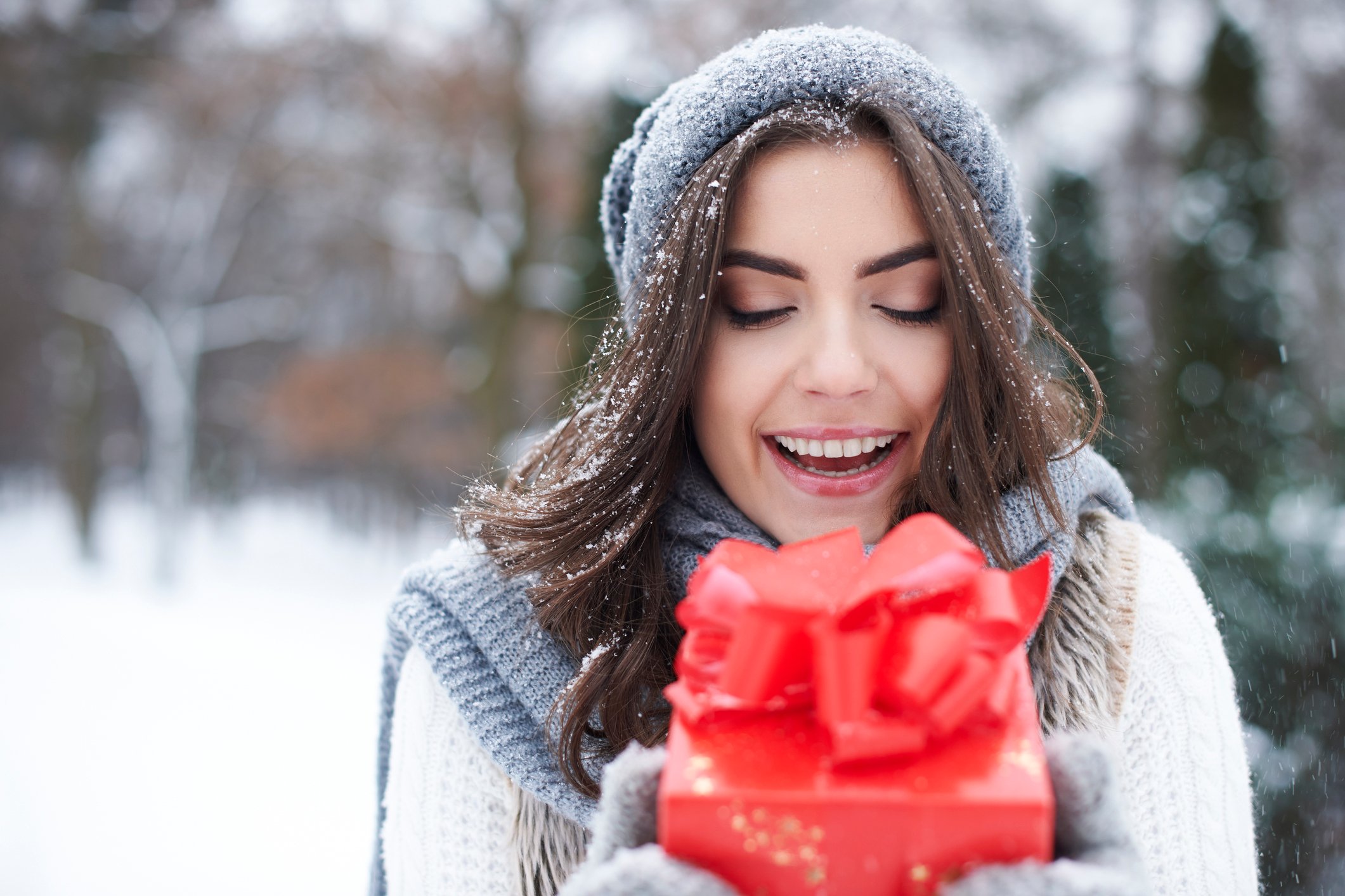 Happy woman standing in the snow holding a red gift box.