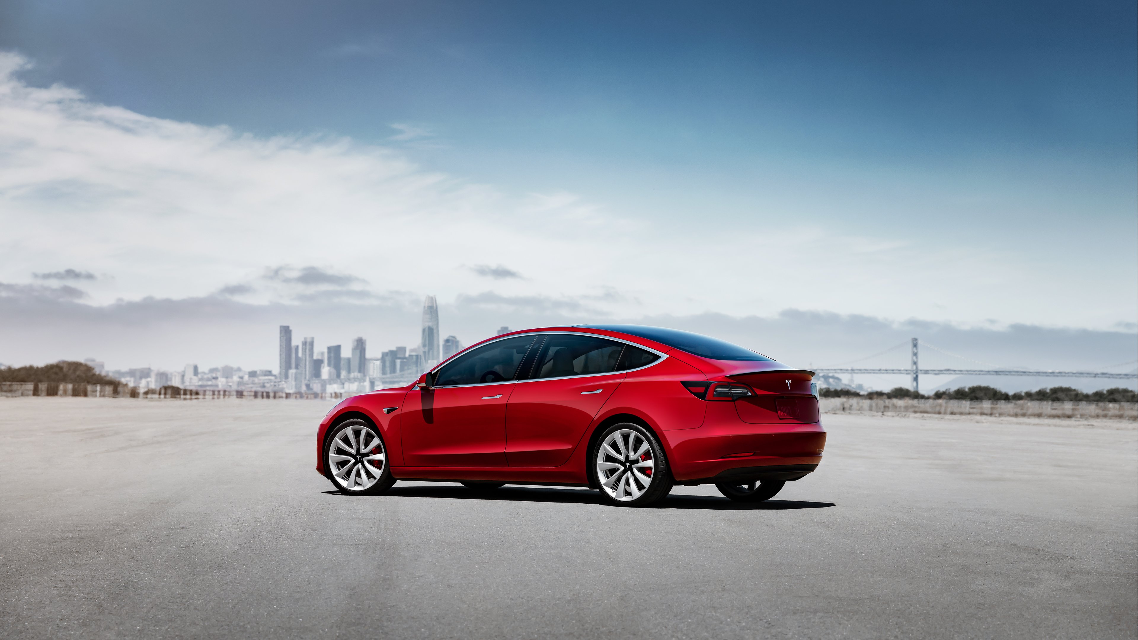 Red Model 3 with a city skyline in the background