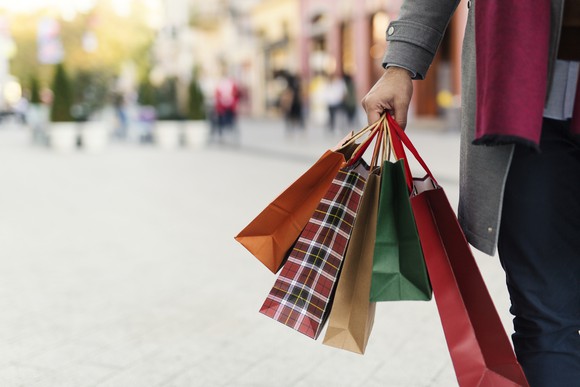 Person walking in an outdoor shopping center and holding multiple shopping bags in his hand.