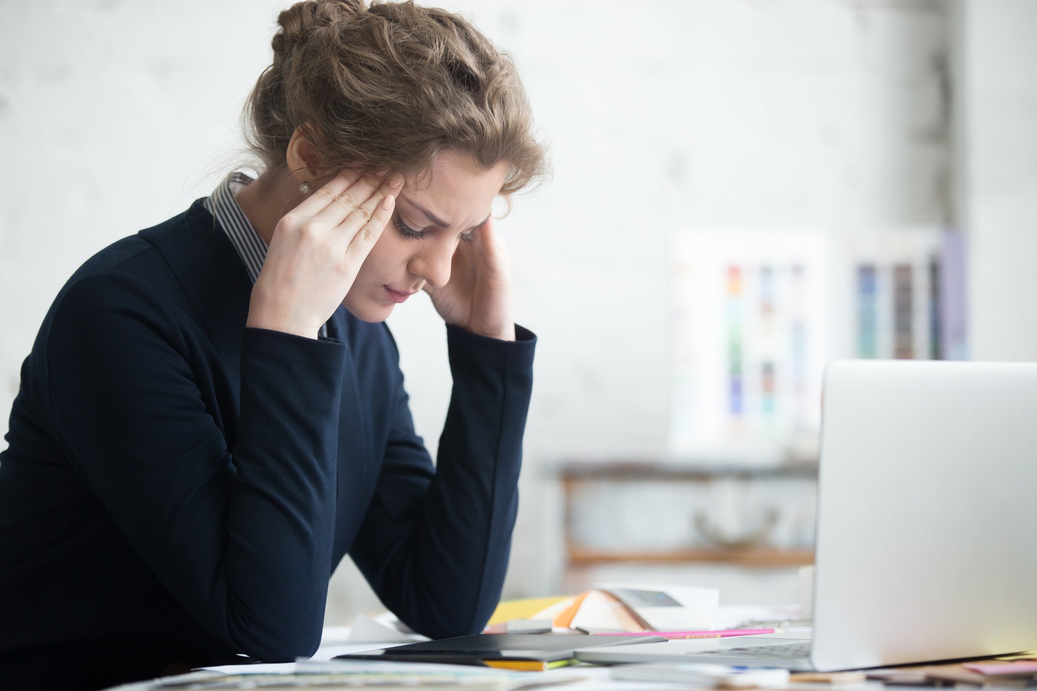 Woman at desk holding her head as if stressed with laptop in front of her