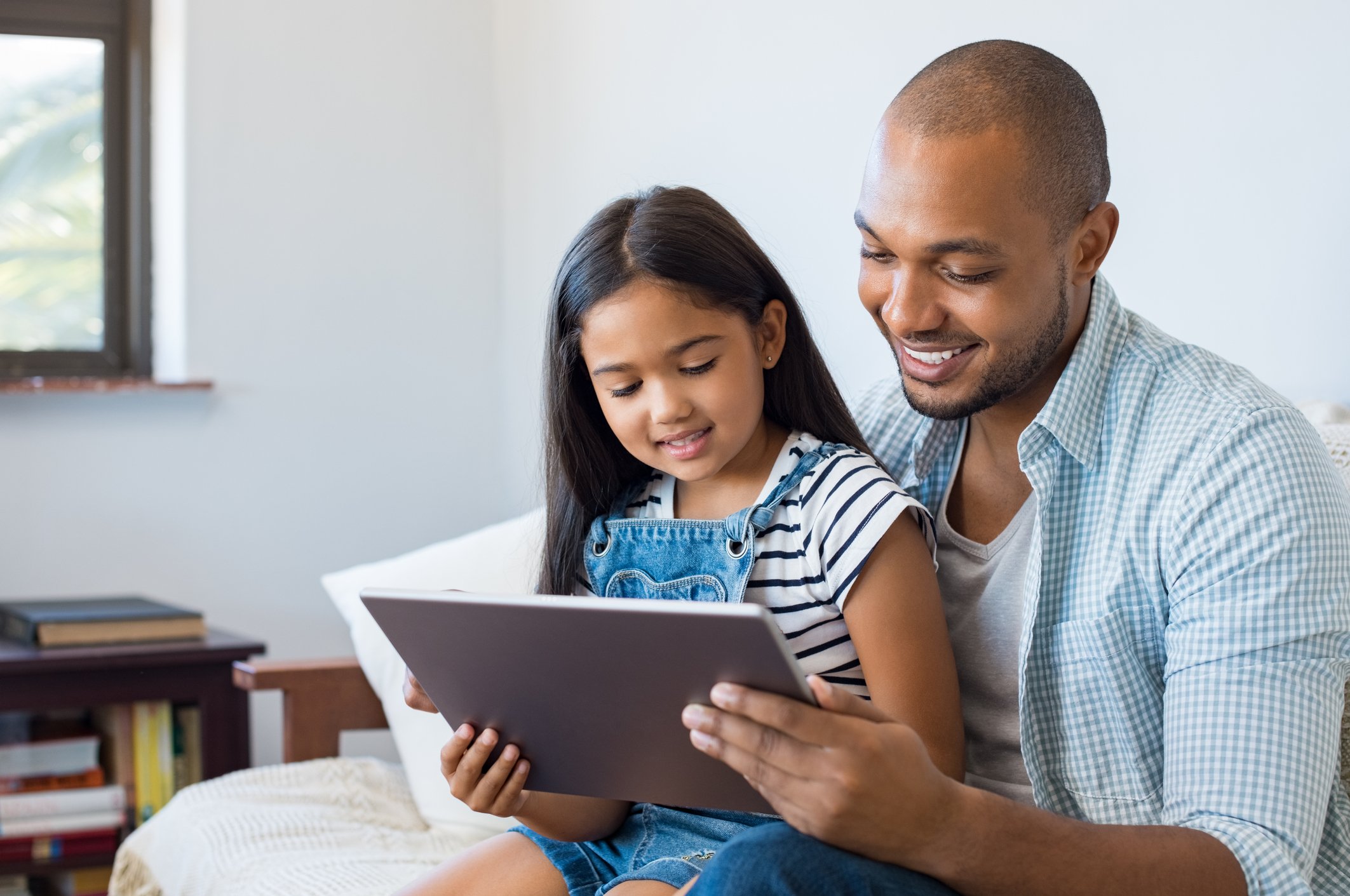 Man holding girl on lap; both are looking at a tablet.