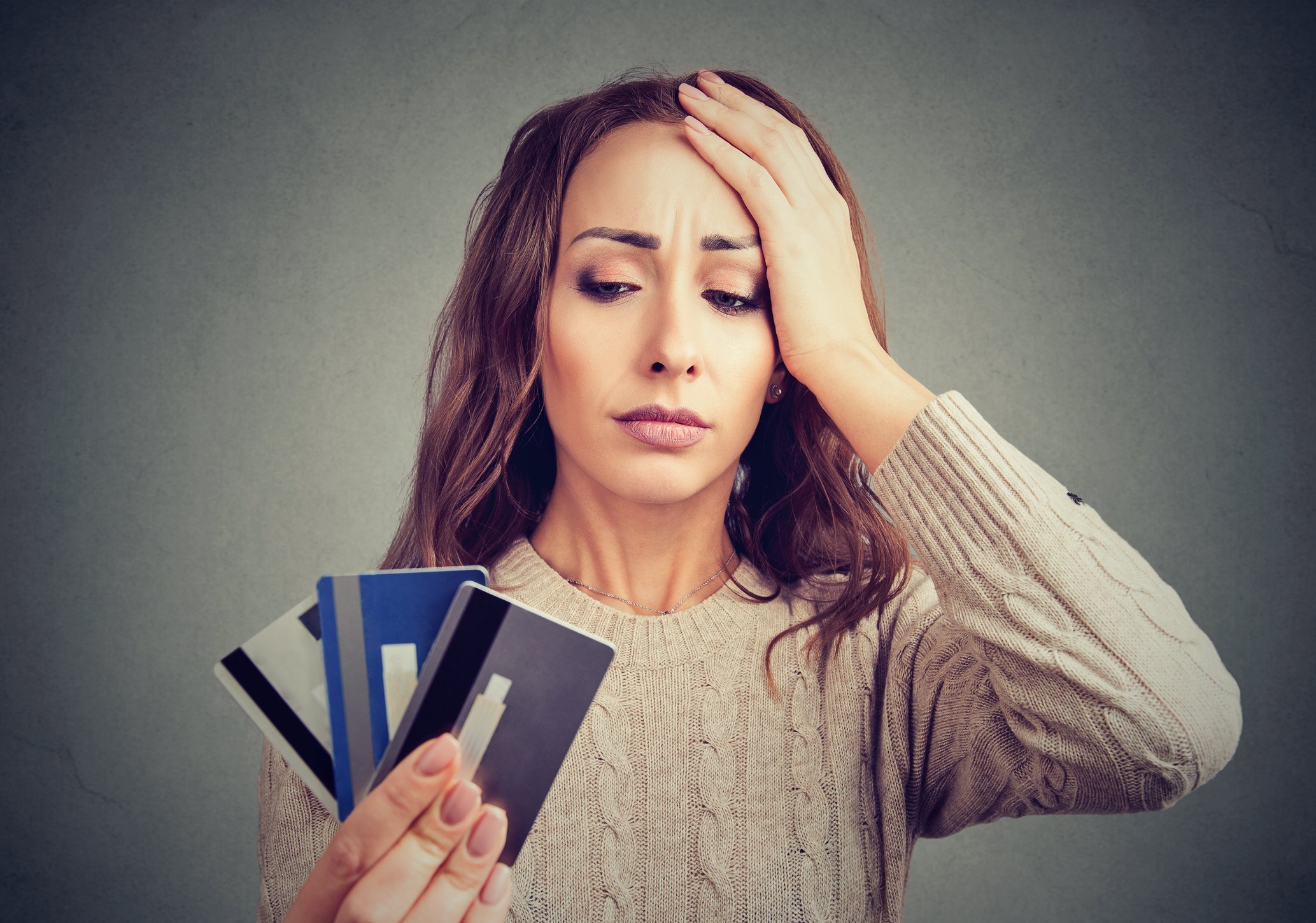 Woman with concerned expression holding her head while holding three credit cards