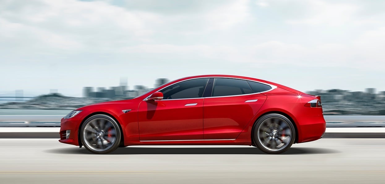 A bright red Tesla Model S, a sleek luxury-sports sedan, on a coastal road.