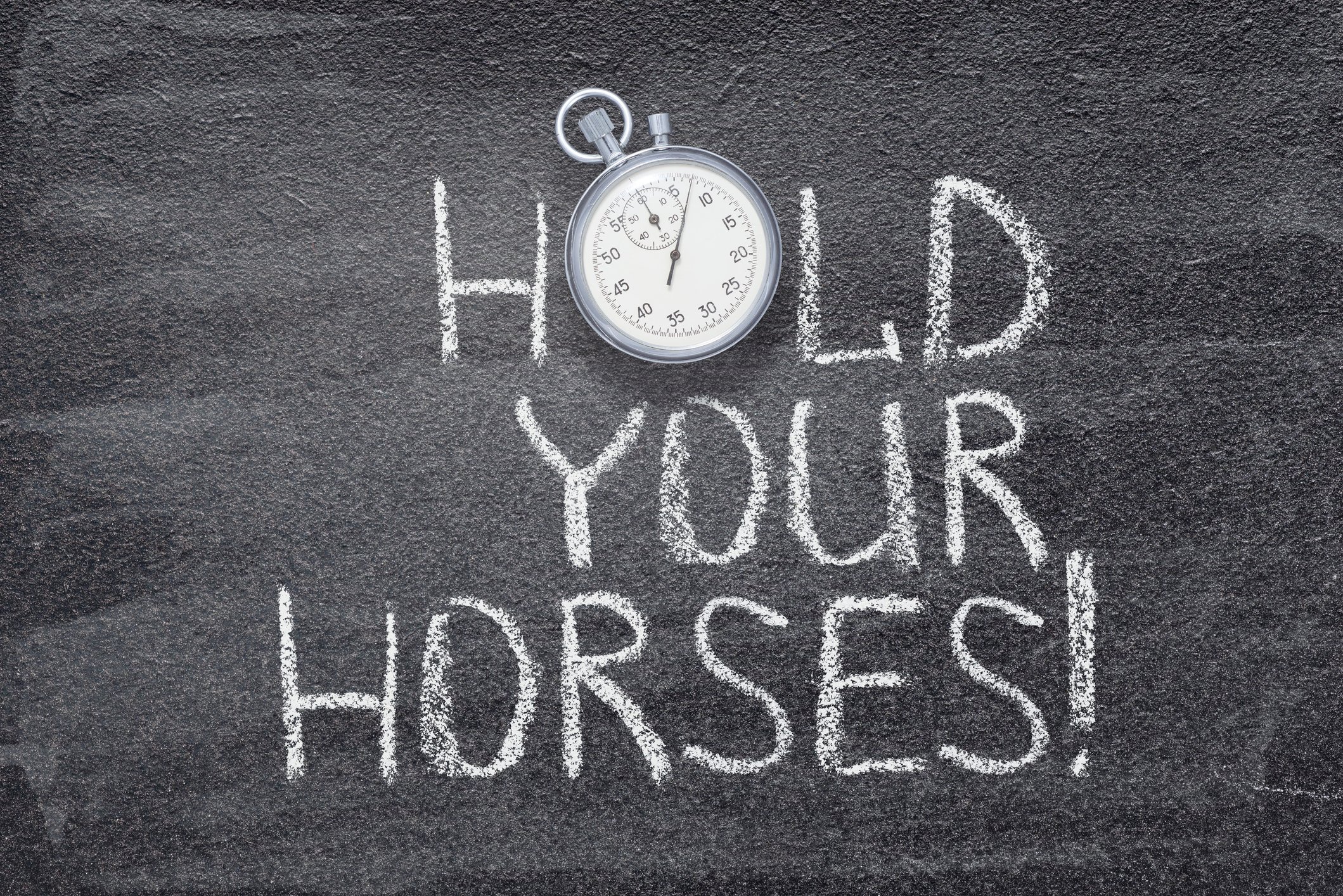 "Hold your horses" written on chalkboard with a vintage stopwatch used instead of O.
