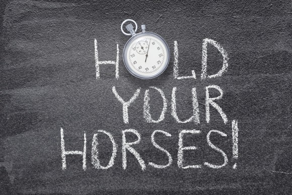 "Hold your horses" written on chalkboard with a vintage stopwatch used instead of O.