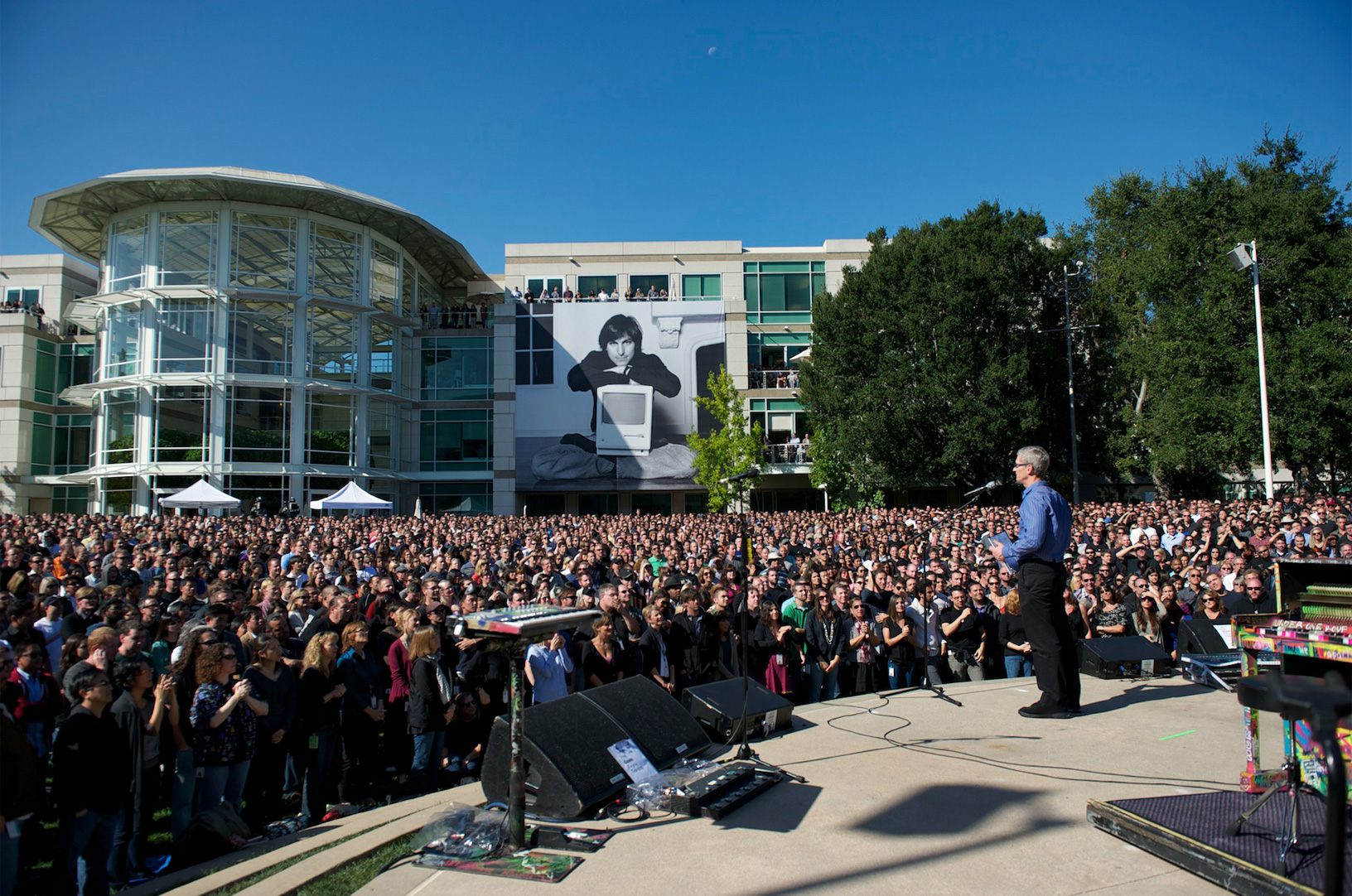 Tim Cook speaks at Apple headquarters with a picture of Jobs in the background.