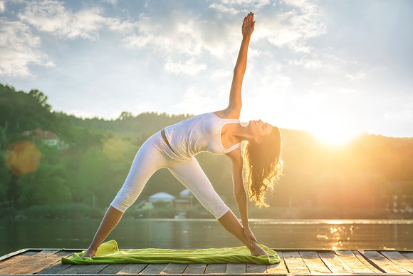 A woman holds a yoga pose with a sunset in the background.